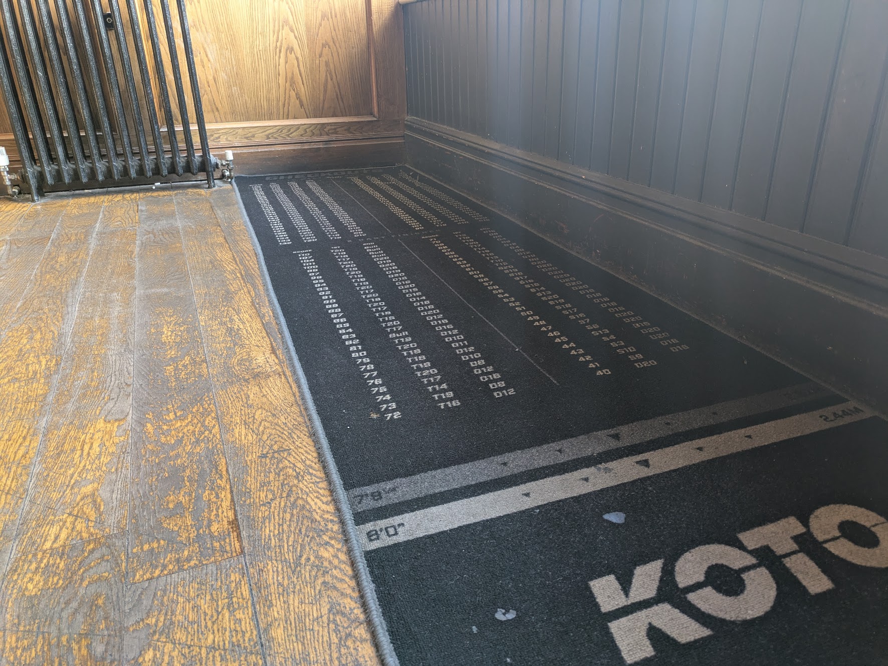 The oche is a mat below the board, with a dense table of numbers showing checkout routes with two or three darts in hand
