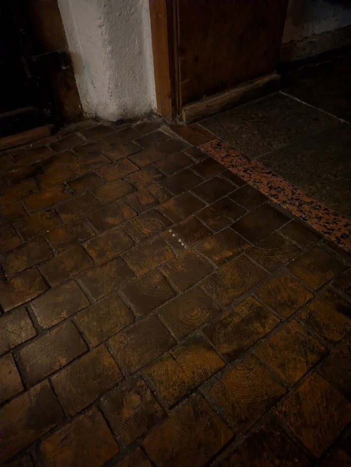 the floor is made of rectangular sections of wooden beams, about 10x15cm. The oche is 5 pins nailed into a tile