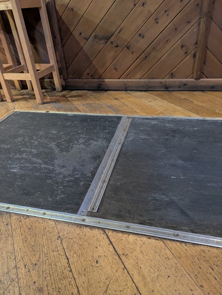 The oche at the duke of york,a black rectangle on the floor with a flat metal strip