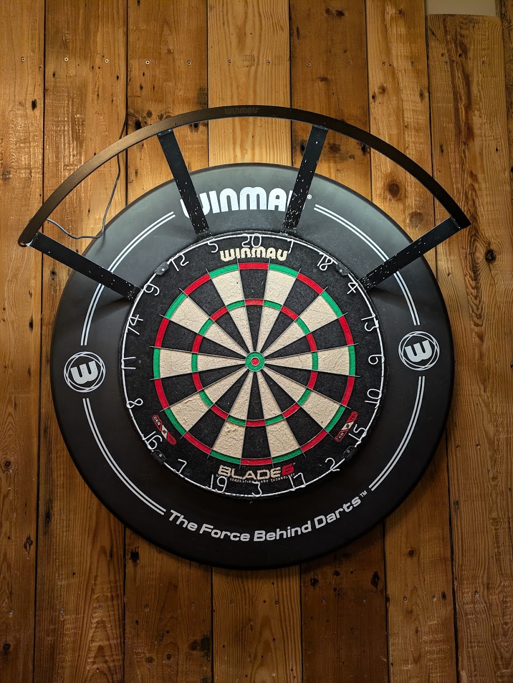 A close up picture of the main dartboard. It is new and fresh looking, with a rustic wooden board backing
