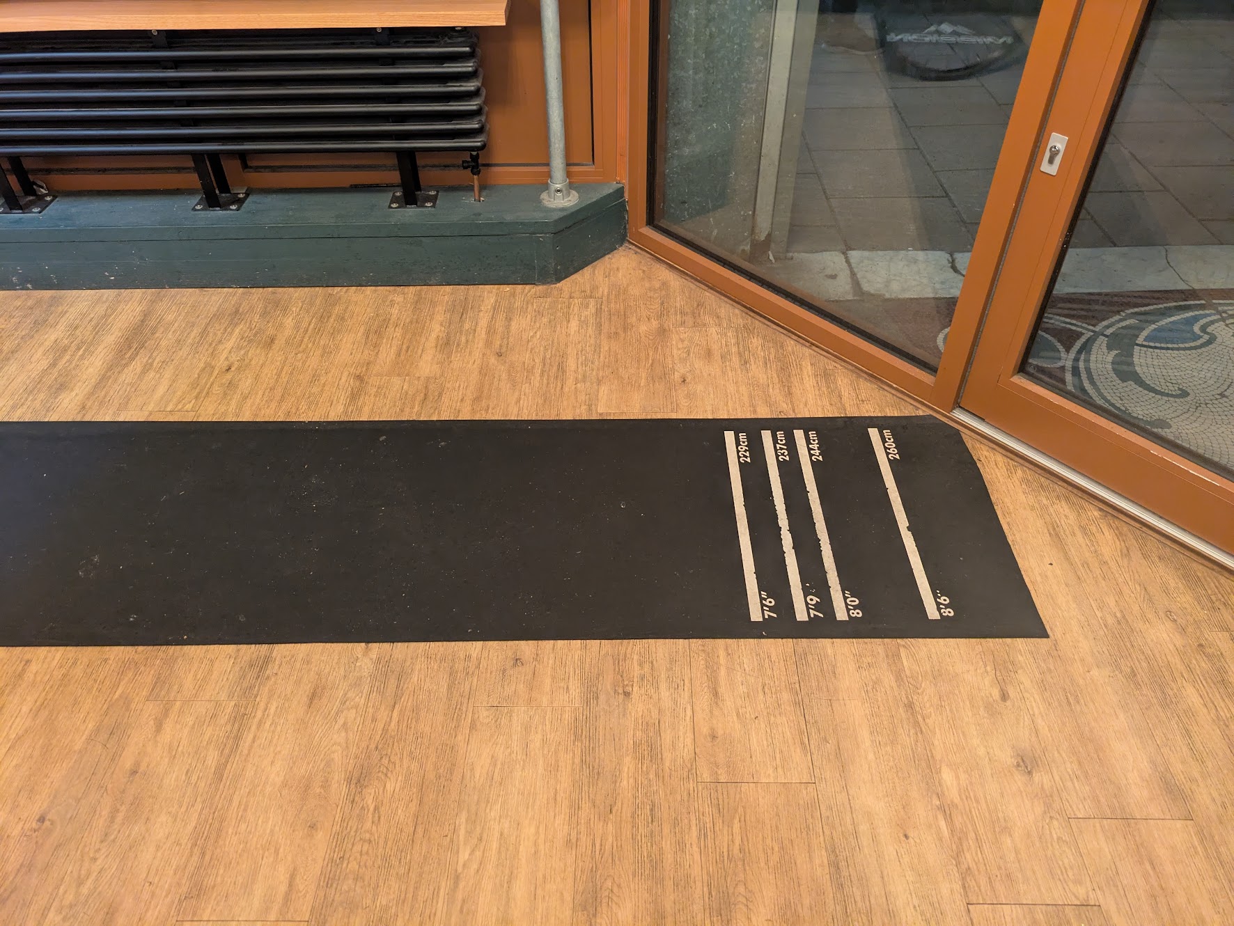 A picture of the oche, which is a mat on the ground with 4 lines at 229cm, 237cm, 244cm and 260cm
