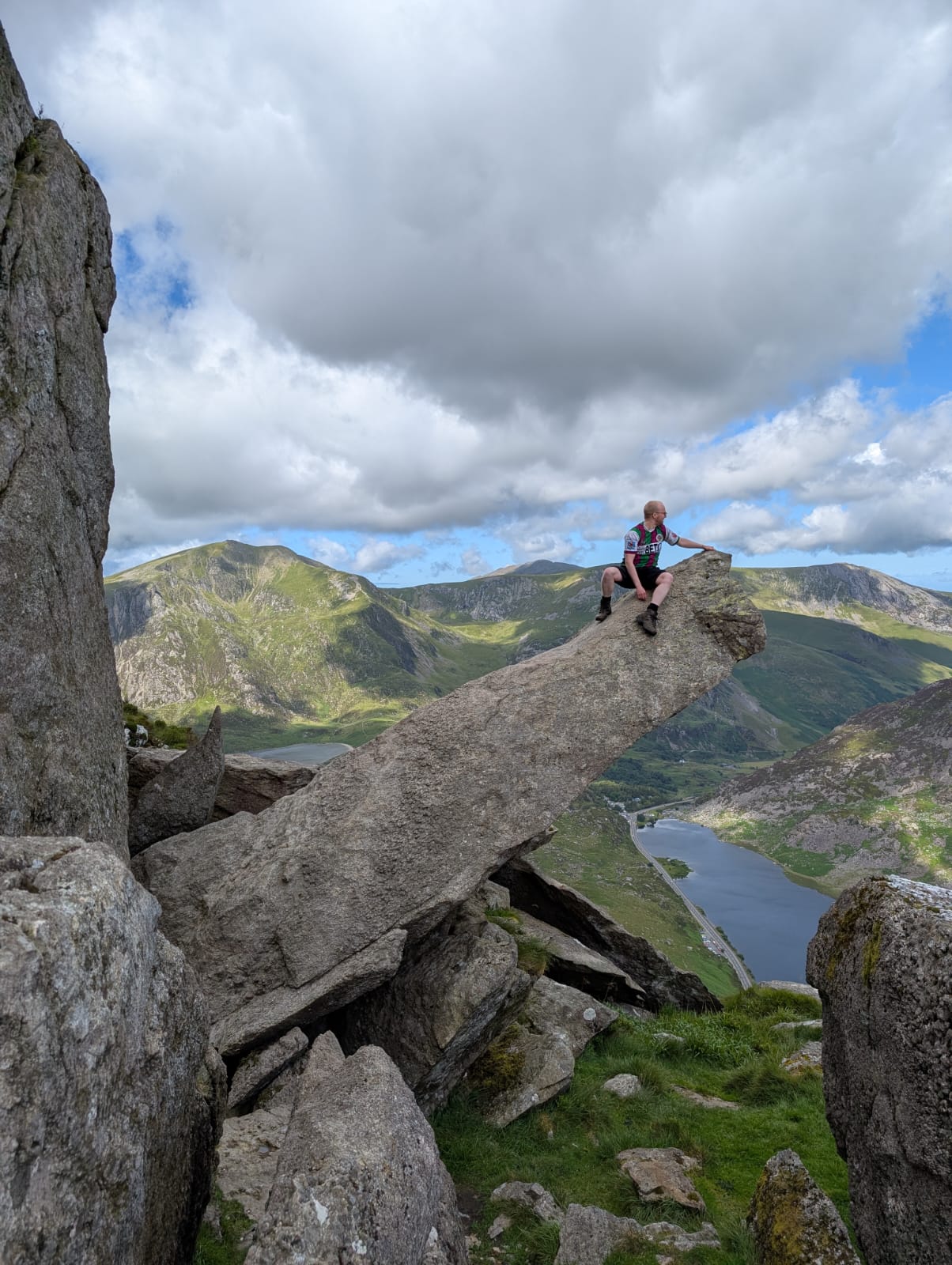 a shot of the mountains, with a lake in the distance below. A large stone protrudes at 45 degrees for a few metres, with me sat at the end of it