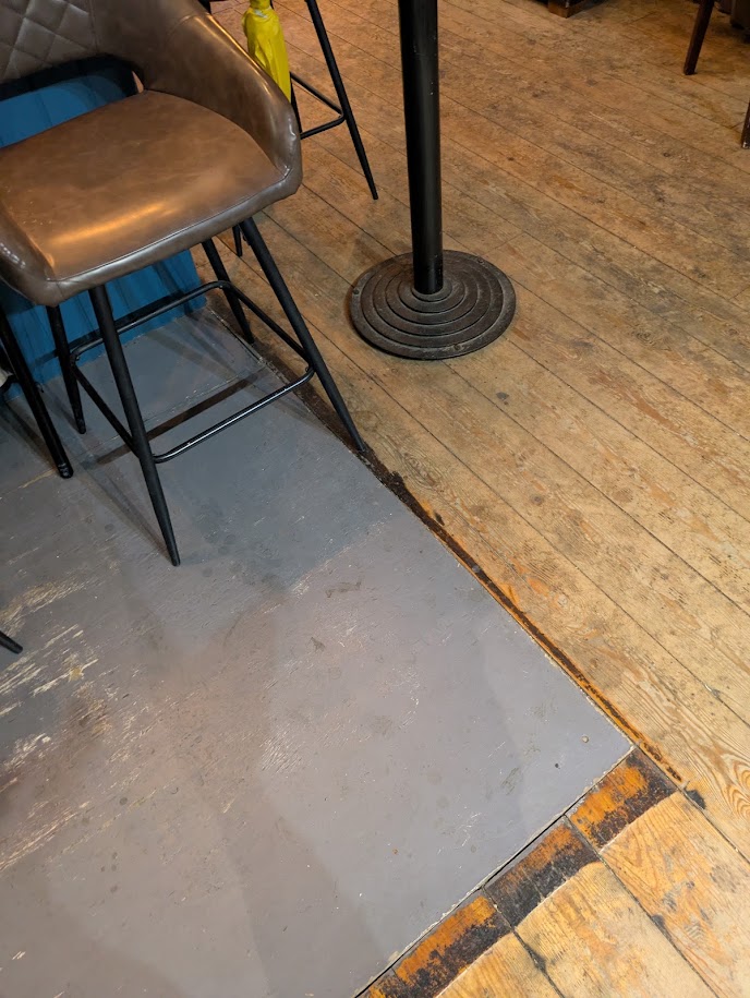 the floor boards stop with a grey board inserted into the floor along the length of the oche