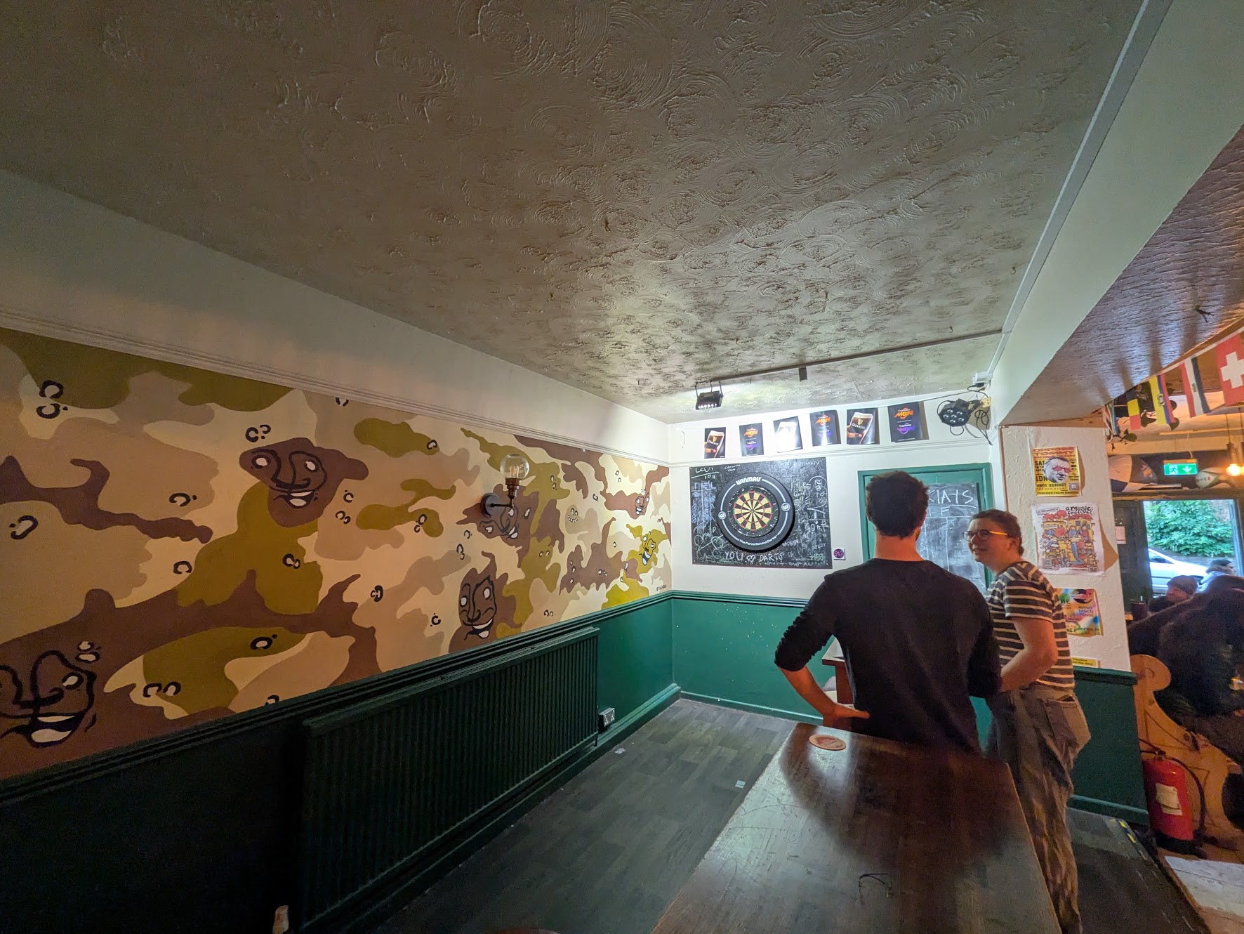 A wide shot of the oche, well lit with high tables forming a barrier to the rest of the pub