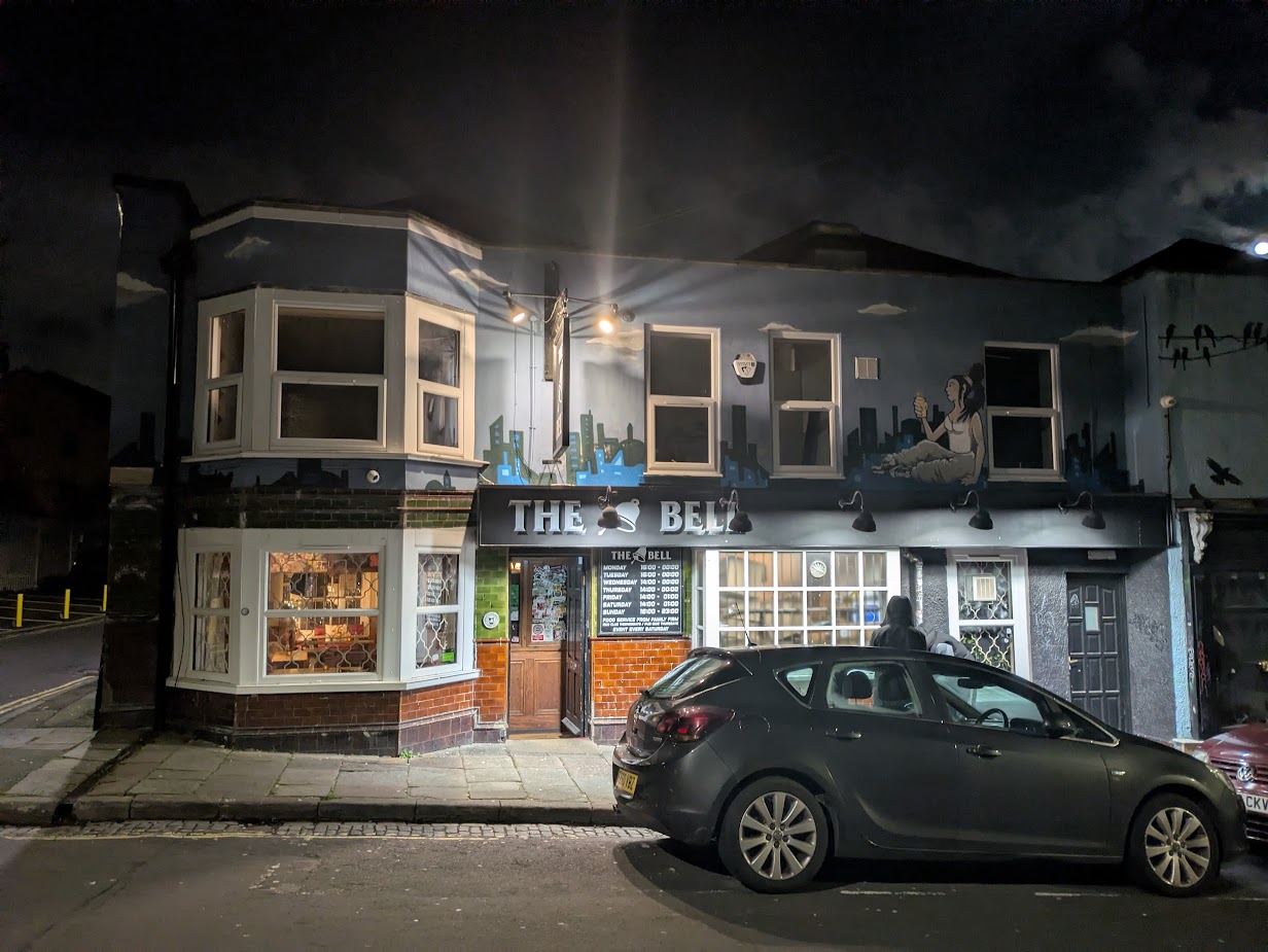 A not very good exterior photo of the Bell at night, with a couple of shady characters loitering outside