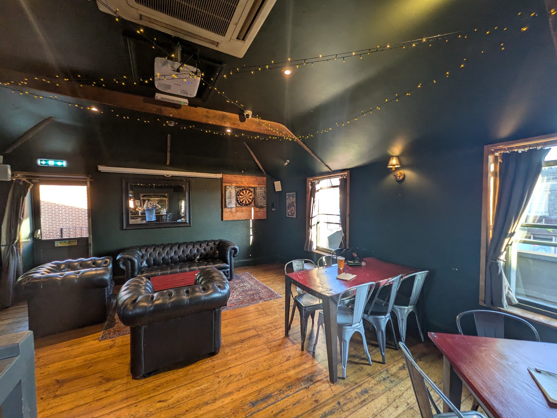 A wide shot showing a room with tables and a couple of sofas next to the oche