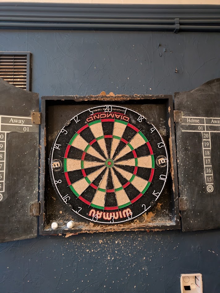 A picture of the board, It's been rotated 180 degrees, looks a bit worse for wear and is in a pretty battered cupboard. There are lots of dart marks in the wall around the cupboard too