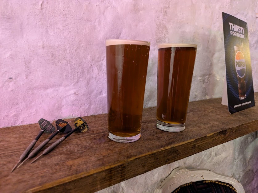 two pints of 6X in unbranded glasses next to a set of darts