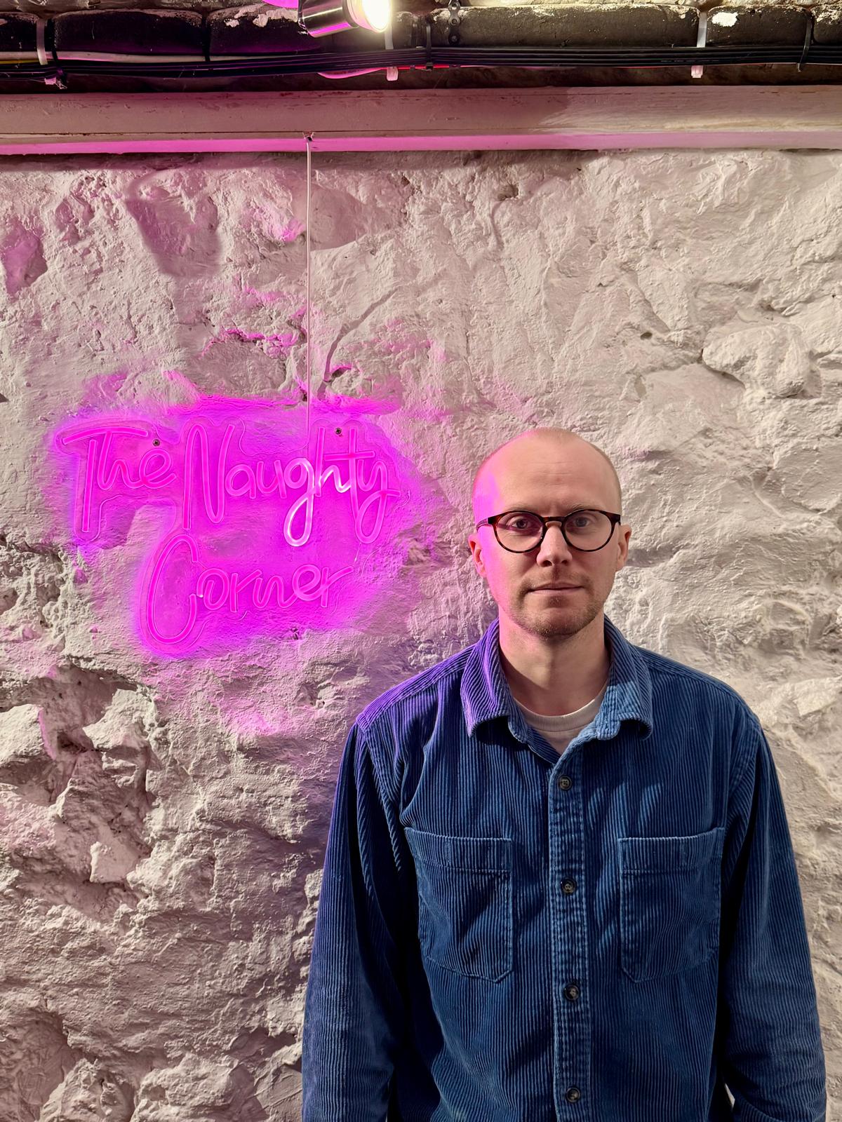A picture of me next to a neon sign saying 'the naughty corner'.